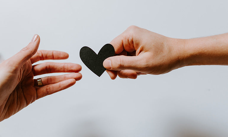 We see two hands, passing a small black paper heart between them.