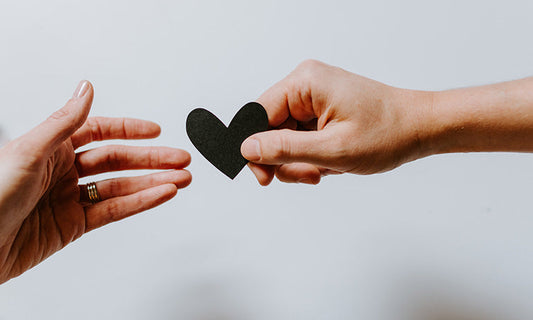 We see two hands, passing a small black paper heart between them.
