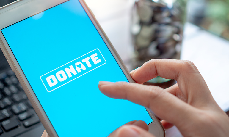 Blue phone screen reading donate with keyboard and jar of coins blurred in background.