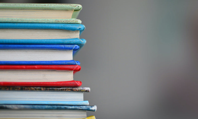 A stack of books viewed from the side so we can see their colourful covers and pages.