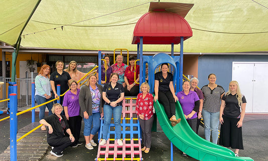 A group of people sit on and stand around a playground. They are all smiling. They are staff at Jumbunna.