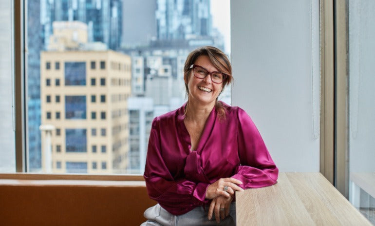 Karina Davis in a red silk shirt smiling with a cityscape in the background.