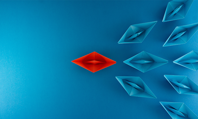 Red origami boat leading a pack of blue origami boats, symbolising leadership.