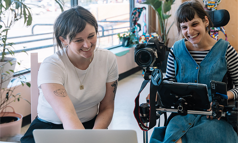 Loom's co-executive director Hannah Reekie (left) with artist Nicole Tsourlenes.|Back of a woman in a wheelchair on stage