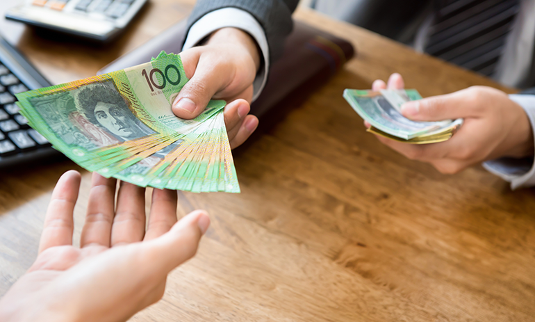 Person in suit handing over a stack of $100 bills to another person.
