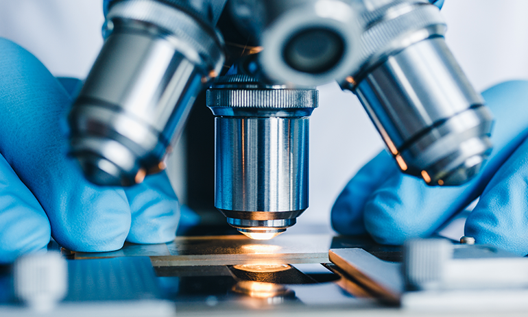 close up of microscpe used by person in blue gloves