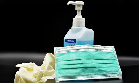 A bottle of hand sanitiser, a blue surgical mask and rubber globes sit on a table.