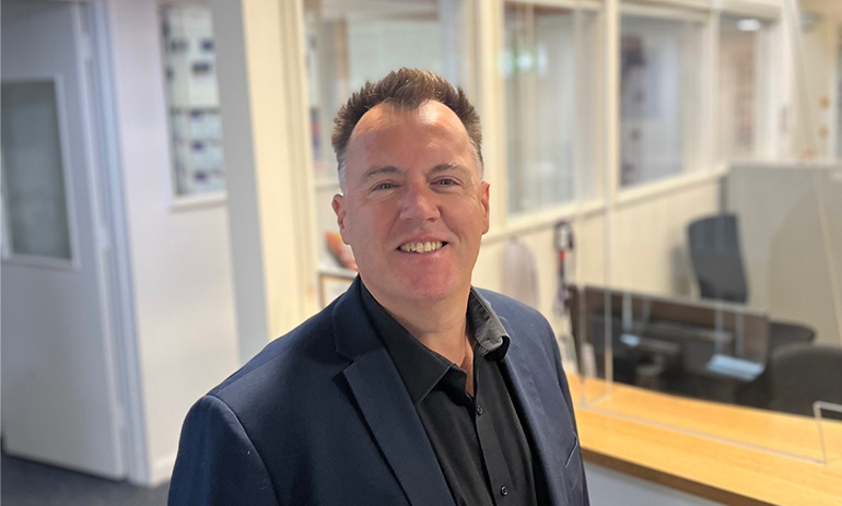 Peter McNamara wears a navy blazer and black shirt, smiling at the camera.|Peter McNamara wears a navy blazer and black shirt, smiling at the camera.