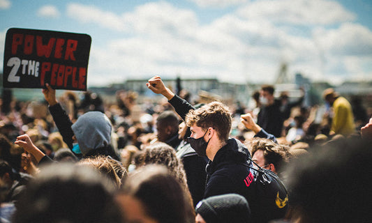 A crowd is protesting. One of them is holding a sign that says 'power 2 the people'|A crowd is protesting. One of them is holding a sign saying 'power 2 the people'