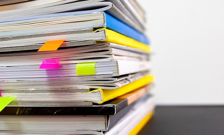 A stack of papers and files, some with colourful sticky tags sticking out of them.