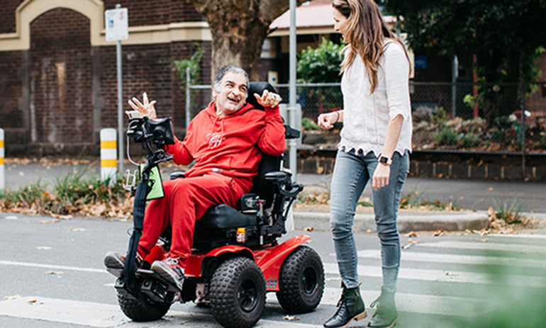 person on a mobility scooter crossing the road while talking to a person walking next to them