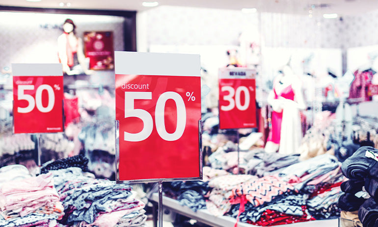 Piles of tables holding clothes with red signs among them saying 50% off