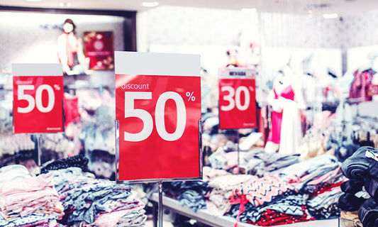Piles of tables holding clothes with red signs among them saying 50% off