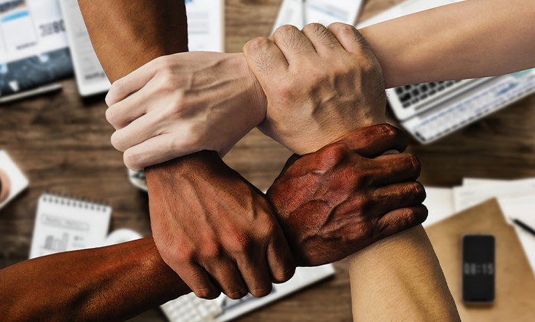 Four people holding each other's wrists in a square. Each one has a slightly darker skin tone.