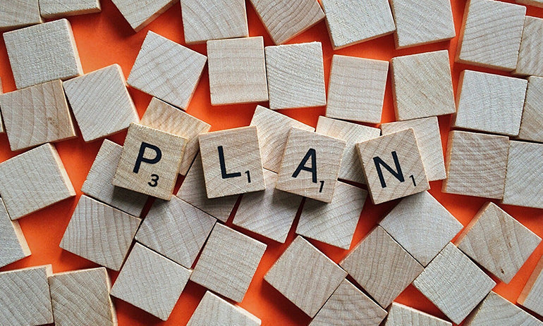 A collection of wooden tiles. Most are facing down but some are facing up to spell out the word 'plan'
