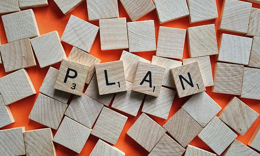 A collection of wooden tiles. Most are facing down but some are facing up to spell out the word 'plan'