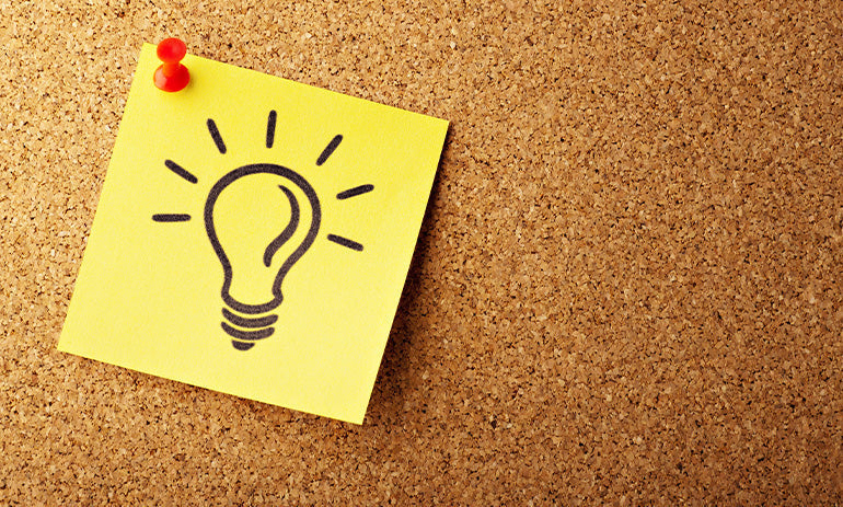 A yellow sticky note with a lightbulb drawn on it in black texta, pinned to a cork board.