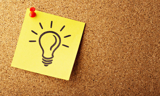 A yellow sticky note with a lightbulb drawn on it in black texta, pinned to a cork board.