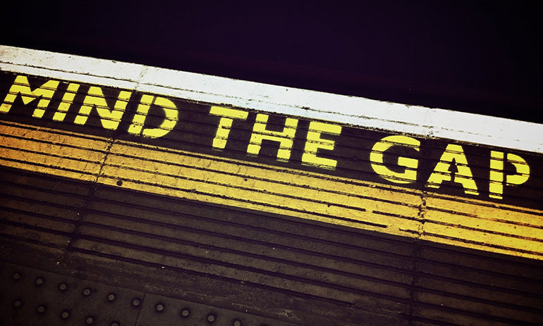 A picture of the warning at the edge of a railway platform that says 'mind the gap' in yellow paint.