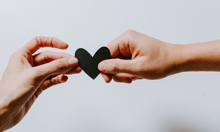 Two people passing a small black paper heart between them. We only see their hands and arms.