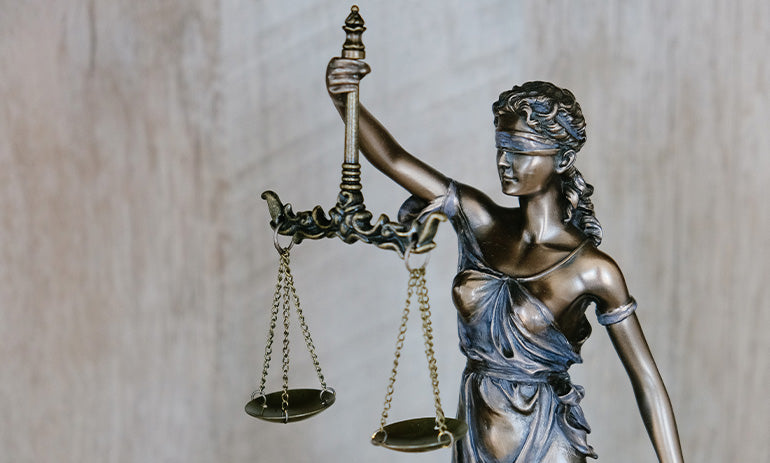 A statue representation of justice, made of a shiny bronze and blue material, blindfolded and holding a set of scales