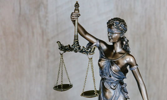 A statue representation of justice, made of a shiny bronze and blue material, blindfolded and holding a set of scales