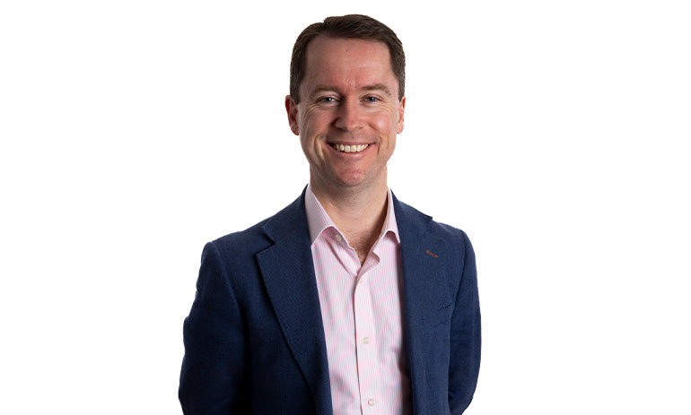 Martin Laverty, a white man with short dark hair, smiles at the camera. He is wearing a pink shirt and navy suit jacket.