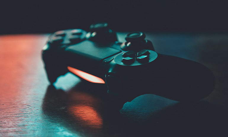 A Playstation controller sitting on a hard surface. The controller is black and is lit up from the side.