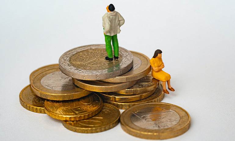 A pile of coins, with two little figurines of a man and a woman sitting on top|A pile of coins, with two little figurines of people sitting on top