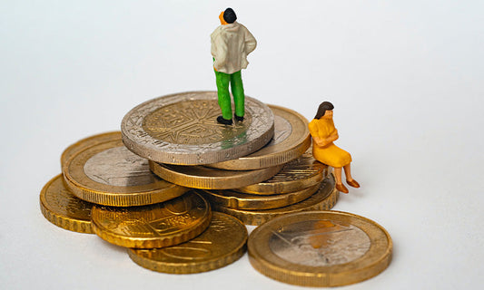 A pile of coins, with two little figurines of a man and a woman sitting on top|A pile of coins, with two little figurines of people sitting on top