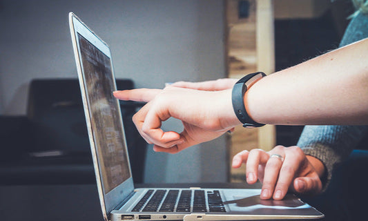 Two people are pointing at and using a laptop. We can only see their arms and hands, and the laptop.|