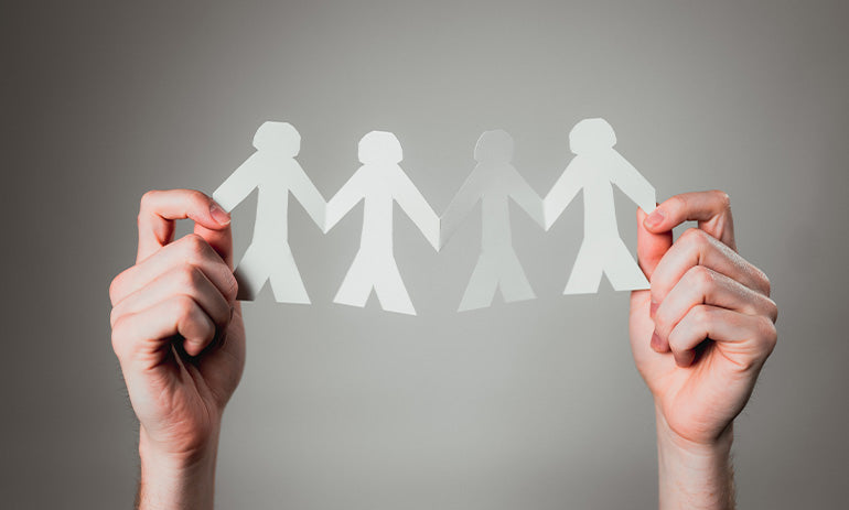 A person's hands holding up a paper cut out of people shaped figures holding hands in a symbol of friendship.