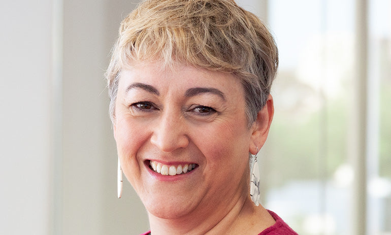 A headshot of Sarah White, who is smiling at the camera. She has short, light hair and drop earrings in a silver colour.