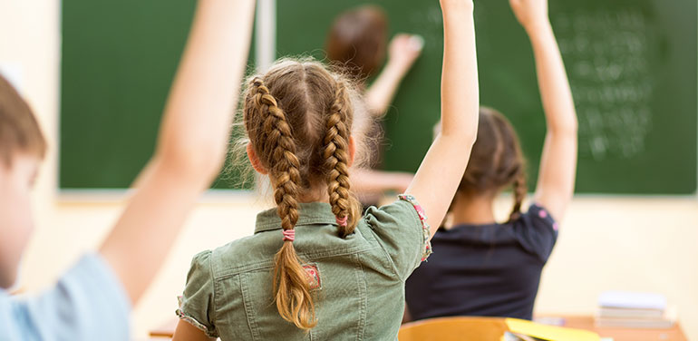 children with their hands raised in class