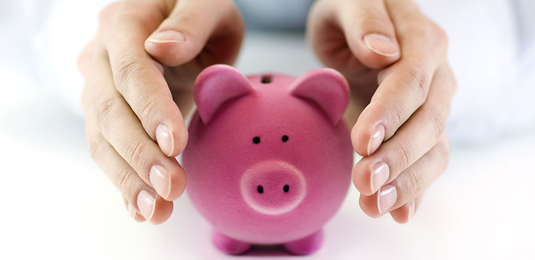 Person putting hands protectively around piggy bank