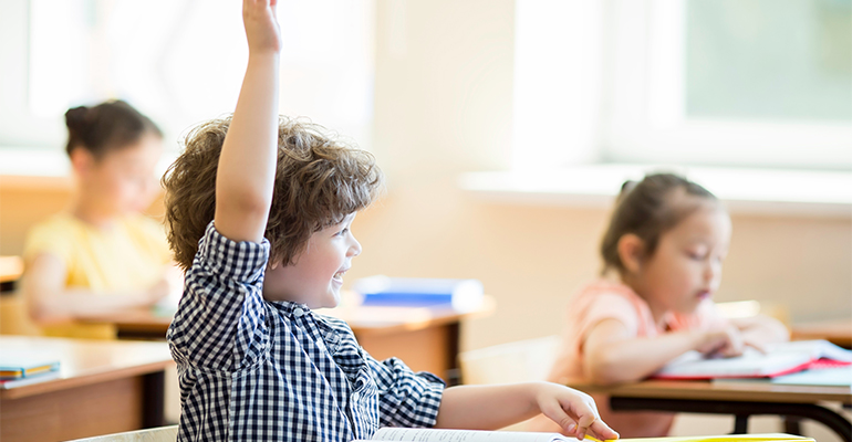 child with hand up in classroom