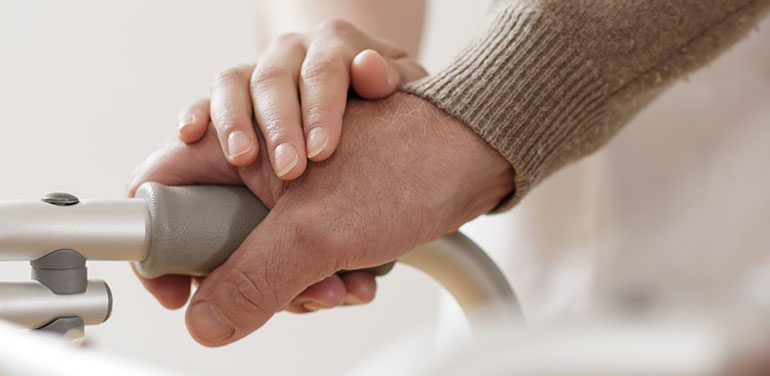 Person resting hand of support on another person's hand on walking frame
