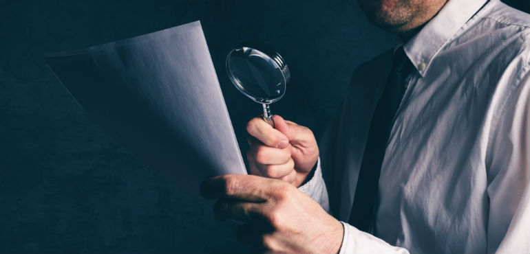 man looking at documents with magnifying glass