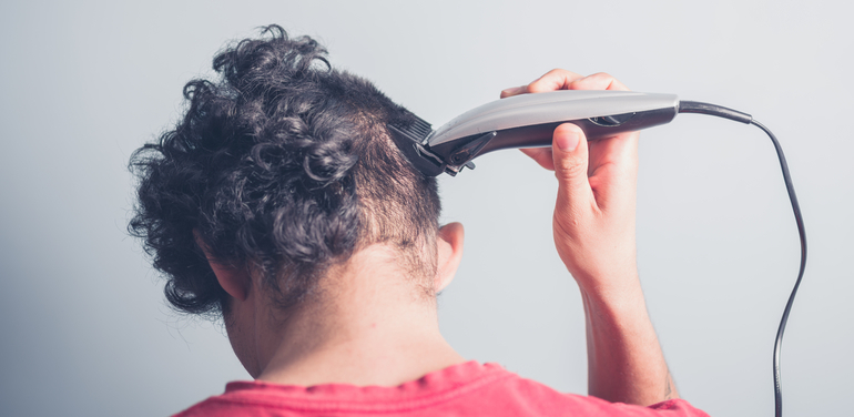 A young man is using hair clippers to give himself a haircut