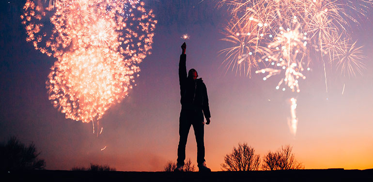 Silhouette of man standing against a night sky full of fireworks
