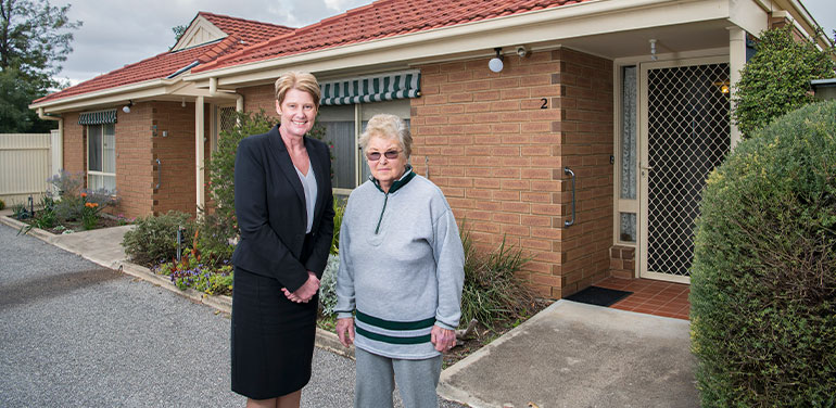 Elderly lady with another woman standing outside a home