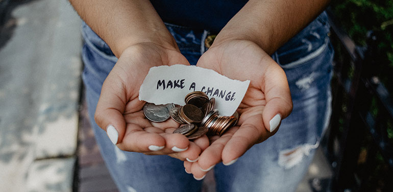 Person holding coins and sign saying make a change