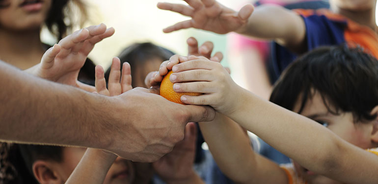 Lots of hands reaching to hold an orange