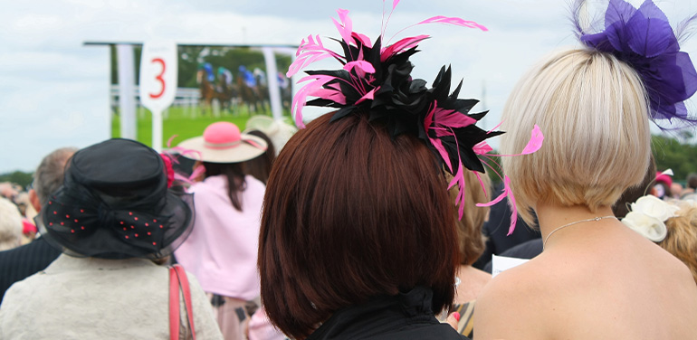 Women in fascinators watching horse racing on a screen