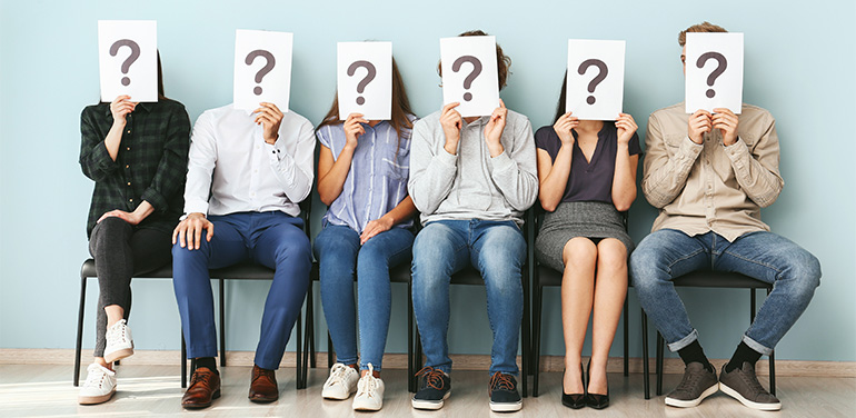 people hiding faces behind paper sheets with question marks while waiting for job interview