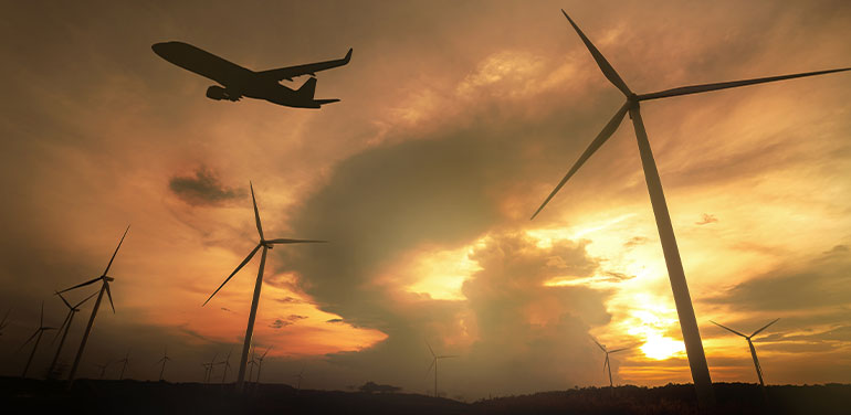 plane flying over wind turbines as the sun sets