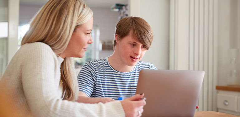 Downs Syndrome man sitting with woman using laptop