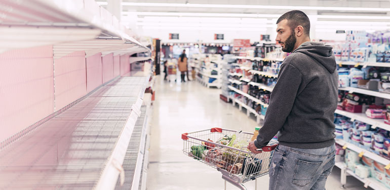 Man with a trolley looking at empty supermarket shelves where toilet paper should be