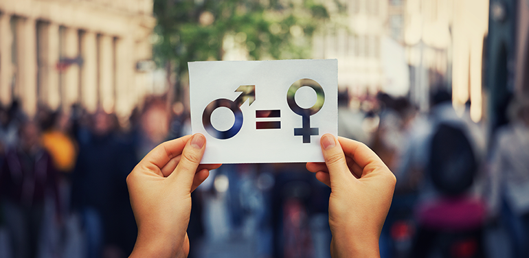 person holding piece of paper with gender symbols on it against the backdrop of a busy street