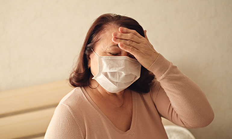 stressed looking older woman wearing a facemask with her hand on her forehead